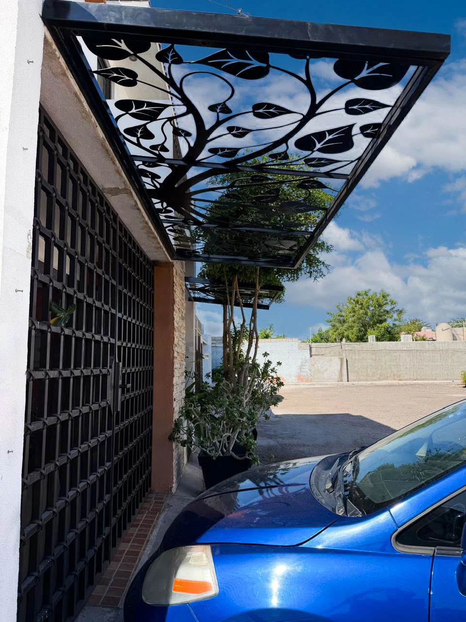 Techo de celosía metálica con diseño de hojas instalado sobre una entrada de casa